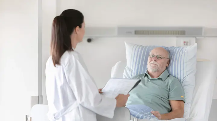 Eine Ärztin unterhält sich mit einem Patienten im Bett.